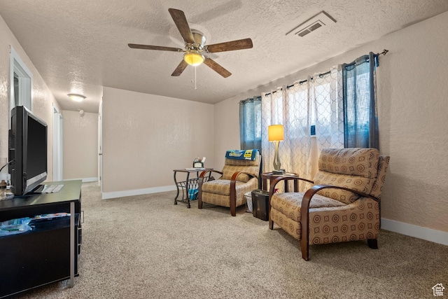 living area featuring a textured ceiling, baseboards, carpet floors, and a ceiling fan