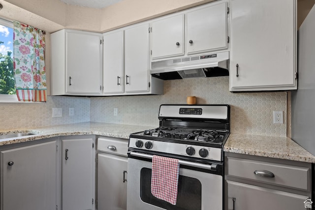 kitchen featuring stainless steel gas range oven, under cabinet range hood, tasteful backsplash, and white cabinetry