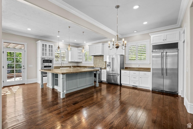 kitchen with built in appliances, white cabinets, a chandelier, dark wood-style flooring, and pendant lighting