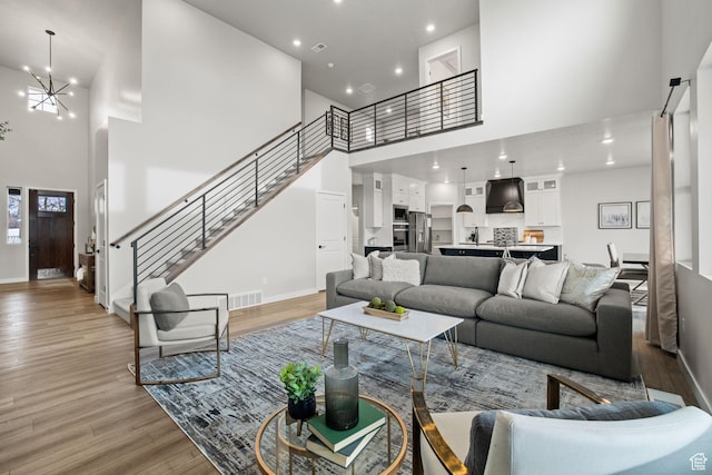 living area featuring a towering ceiling, light wood-type flooring, baseboards, a chandelier, and stairway