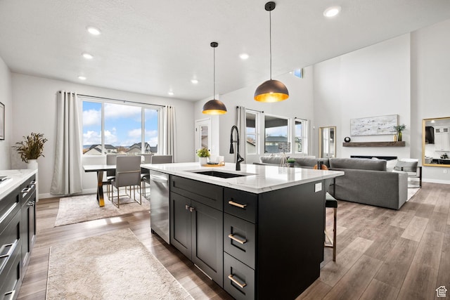 kitchen with a sink, dark cabinets, dishwasher, light wood finished floors, and recessed lighting