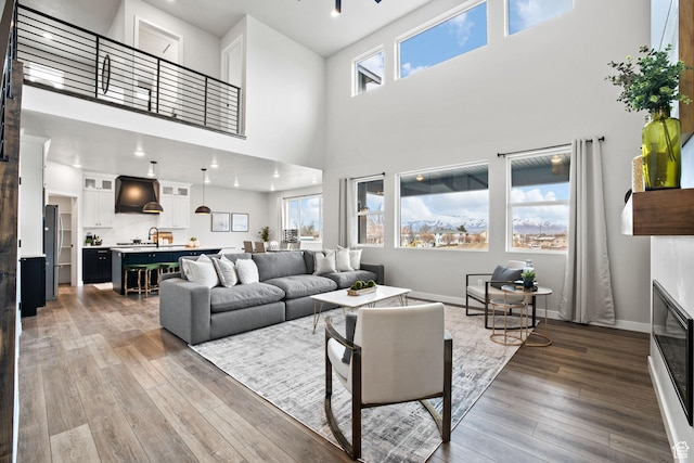 living room with wood finished floors, a towering ceiling, a glass covered fireplace, baseboards, and recessed lighting