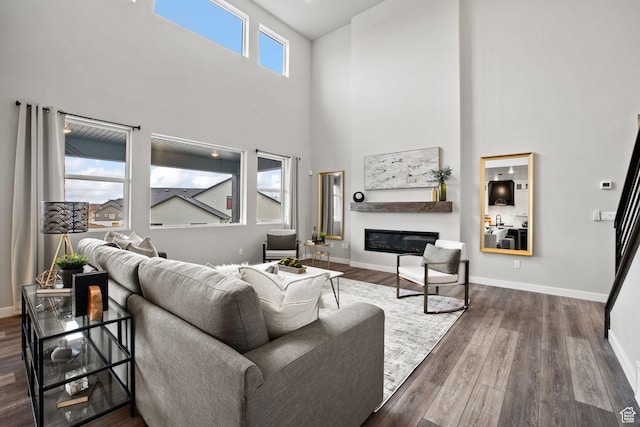 living room with dark wood-style floors, a high ceiling, a glass covered fireplace, and baseboards
