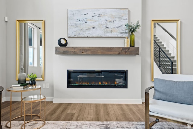 living area with wood finished floors, a glass covered fireplace, baseboards, and stairway
