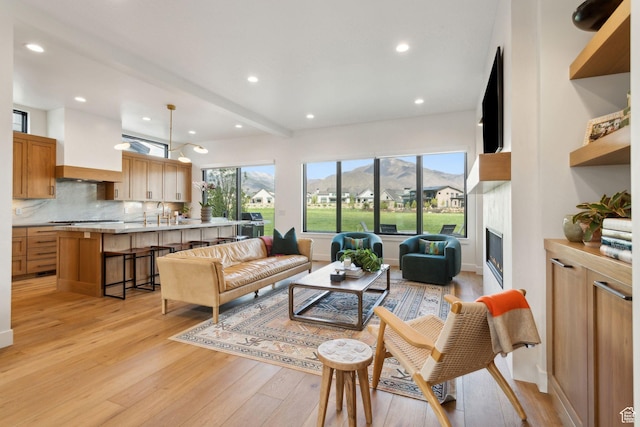 living area with light wood-style floors, a glass covered fireplace, recessed lighting, and baseboards