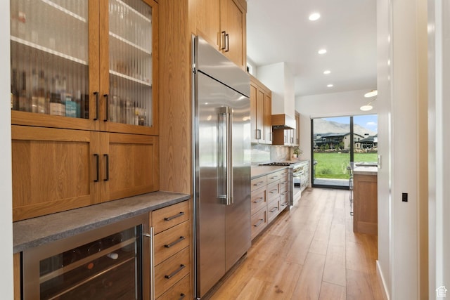 kitchen featuring premium appliances, wine cooler, light wood finished floors, glass insert cabinets, and recessed lighting