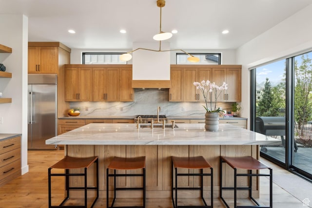 kitchen with built in fridge, decorative backsplash, a sink, light stone counters, and light wood-style flooring