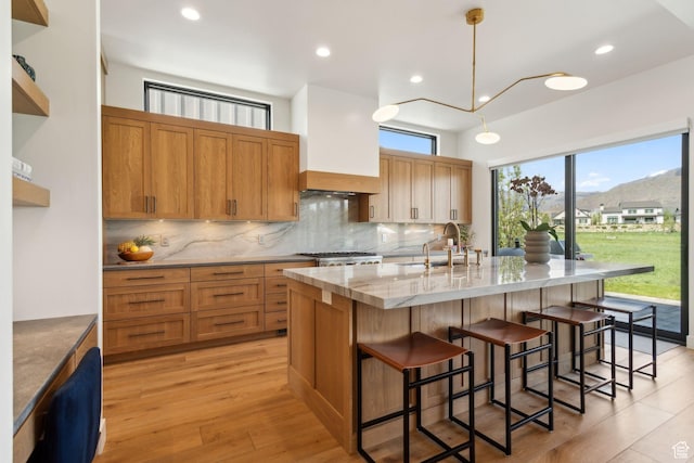 kitchen featuring a sink, tasteful backsplash, an island with sink, a kitchen bar, and light stone counters