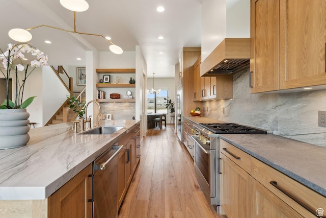 kitchen with high quality appliances, a sink, wall chimney range hood, open shelves, and light wood-type flooring