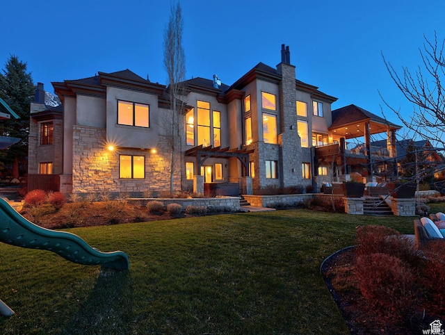 back of house with stone siding, stucco siding, a yard, and a pergola