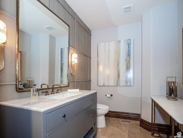 bathroom featuring baseboards, toilet, vanity, and stone finish flooring