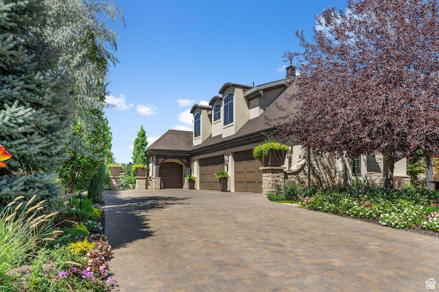 view of front of property with an attached garage, stone siding, stucco siding, and decorative driveway