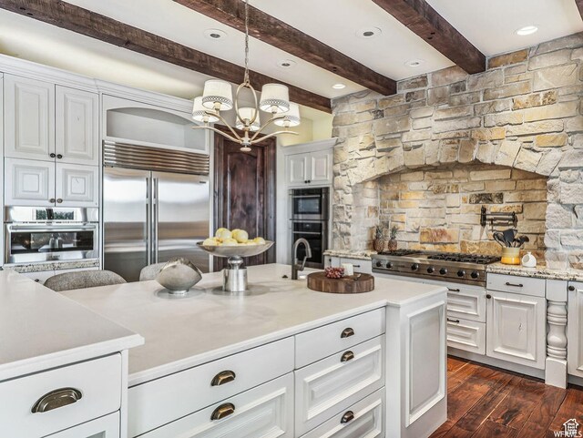 kitchen with appliances with stainless steel finishes, dark wood-style floors, a chandelier, white cabinets, and beamed ceiling