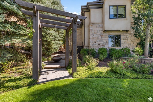 back of house with stucco siding, stone siding, a pergola, a lawn, and a patio area