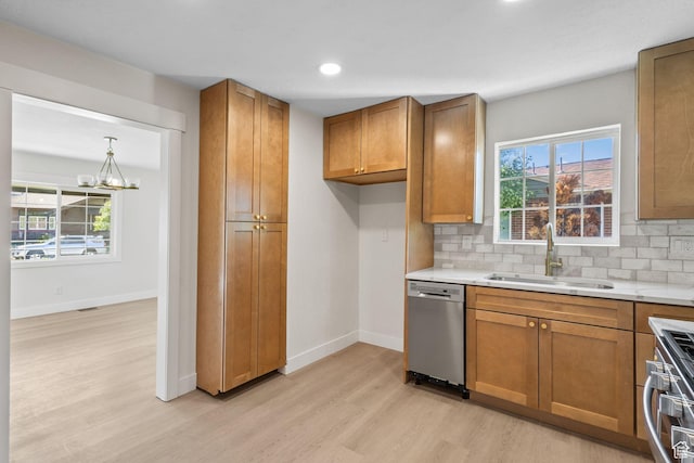 kitchen with stainless steel appliances, a sink, light wood finished floors, brown cabinetry, and light countertops