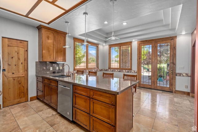 kitchen with stainless steel dishwasher, a sink, a peninsula, a raised ceiling, and brown cabinetry