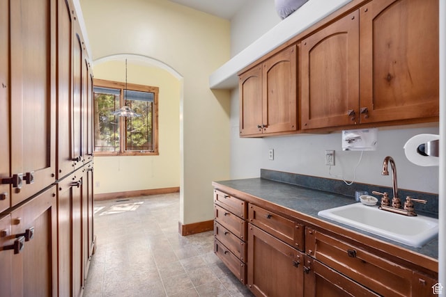 kitchen featuring dark countertops, a sink, decorative light fixtures, baseboards, and brown cabinets