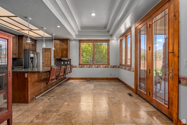 kitchen featuring stainless steel refrigerator with ice dispenser, baseboards, tasteful backsplash, a tray ceiling, and a sink