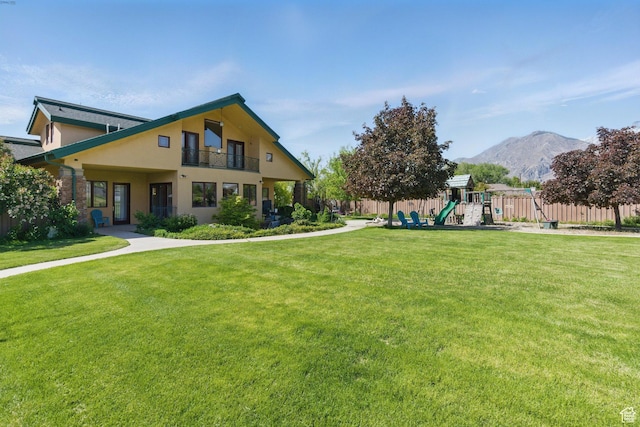 view of front of house featuring a playground, a mountain view, a balcony, and stucco siding