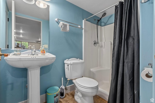 bathroom featuring a shower stall, toilet, baseboards, and a sink