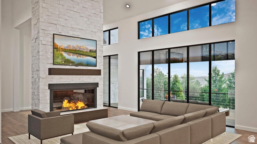 living room with baseboards, healthy amount of natural light, wood finished floors, a stone fireplace, and a towering ceiling