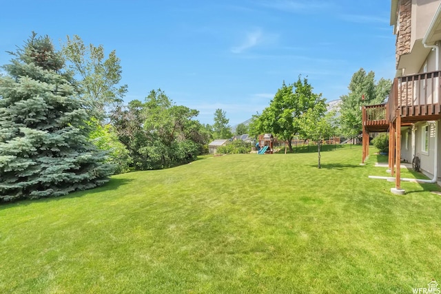 view of grassy yard with a playground and a wooden deck