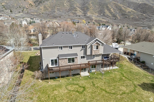 back of house with stucco siding, a deck with mountain view, a chimney, stone siding, and a residential view