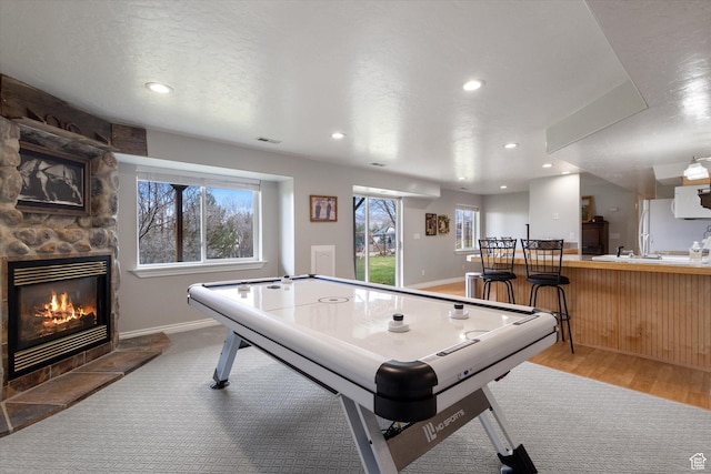 game room featuring recessed lighting, a stone fireplace, baseboards, and wood finished floors