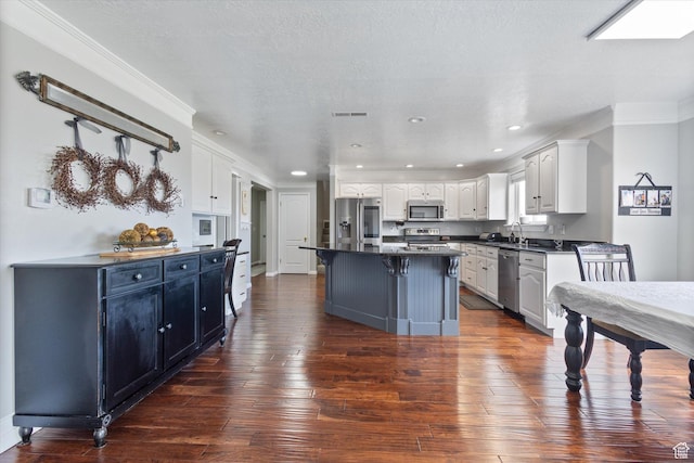 kitchen with appliances with stainless steel finishes, dark countertops, white cabinets, ornamental molding, and dark wood finished floors
