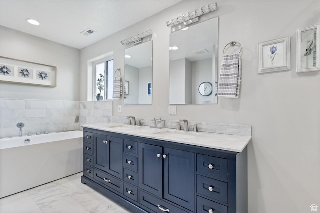 full bathroom featuring marble look tiles, a freestanding tub, double vanity, and recessed lighting