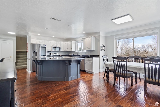 kitchen with appliances with stainless steel finishes, dark countertops, white cabinetry, a textured ceiling, and a kitchen island