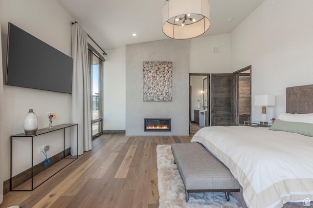 bedroom with wood finished floors, a glass covered fireplace, and baseboards