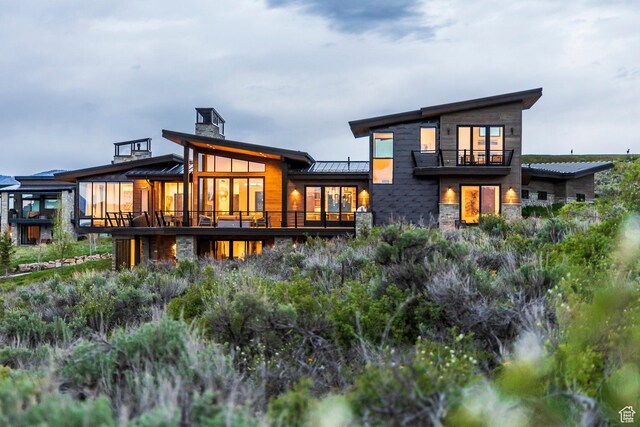 6110 E Blue Wing Loop, Kamas, UT 84036 - rear view of house with a standing seam roof, stone siding, a balcony, metal roof, and a chimney