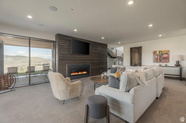 living room featuring light colored carpet, recessed lighting, a large fireplace, and stairs
