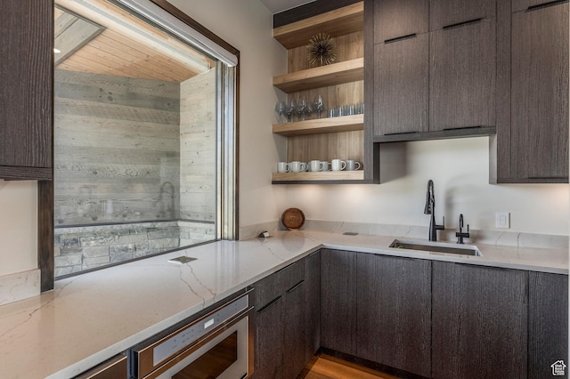 kitchen with a sink, open shelves, stainless steel microwave, light stone counters, and modern cabinets