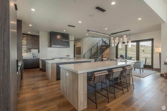 kitchen with a large island, modern cabinets, hardwood / wood-style flooring, wall chimney range hood, and recessed lighting