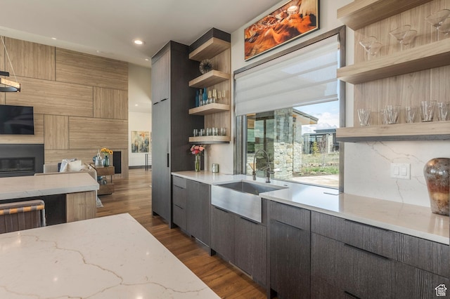 kitchen featuring open shelves, a sink, open floor plan, dark wood finished floors, and light stone countertops