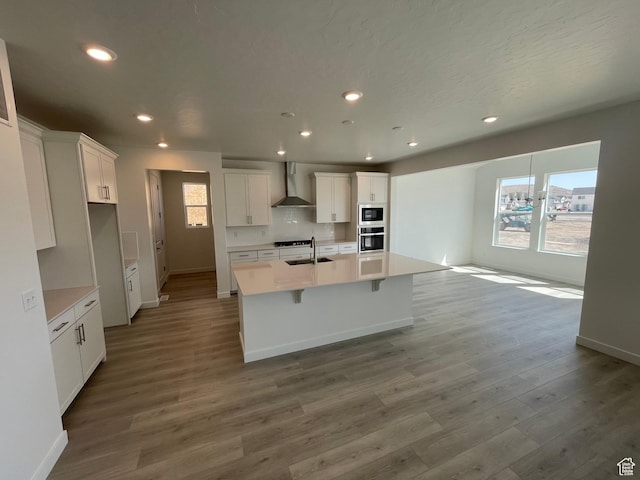 kitchen with wall chimney range hood, built in microwave, baseboards, plenty of natural light, and recessed lighting