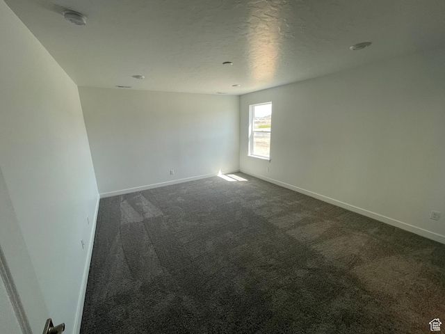 spare room featuring dark carpet, baseboards, a smoke detector, and a textured ceiling
