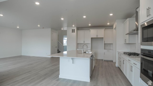 5488 N Trailside Unit 431, Eagle Mountain, UT 84005 - kitchen featuring stainless steel appliances, a sink, an island with sink, light wood-style floors, and wall chimney range hood
