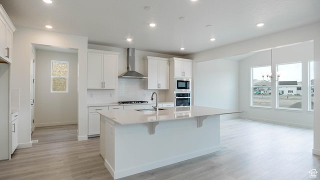 5488 N Trailside Unit 431, Eagle Mountain, UT 84005 - kitchen featuring wall chimney range hood, stainless steel appliances, a kitchen island with sink, light wood-style flooring, and decorative backsplash
