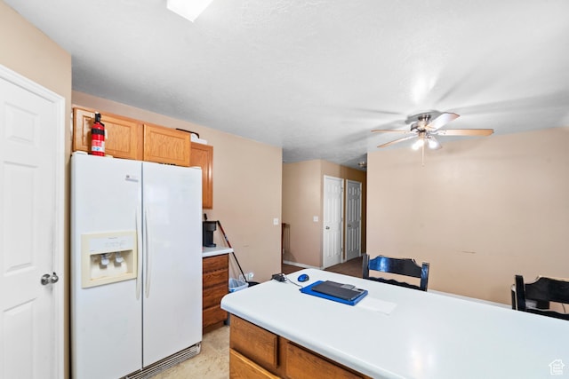 kitchen with white fridge with ice dispenser, a ceiling fan, light countertops, and brown cabinets