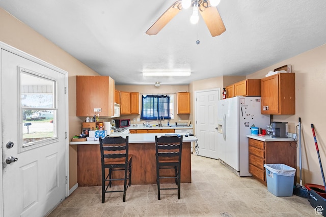 kitchen featuring white appliances, a peninsula, light countertops, ceiling fan, and a kitchen bar