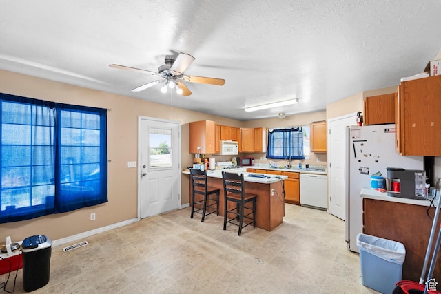 kitchen with white appliances, a peninsula, a kitchen bar, a ceiling fan, and light countertops