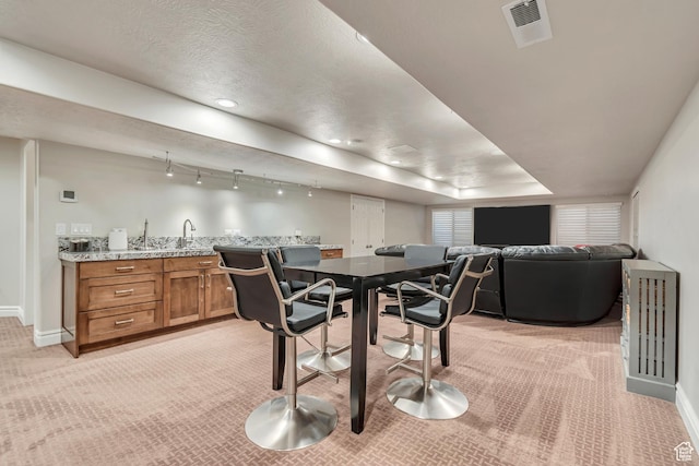 dining space with light colored carpet, baseboards, and bar with sink