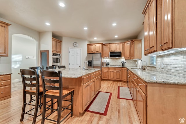 kitchen with appliances with stainless steel finishes, a sink, light wood-style flooring, backsplash, and arched walkways