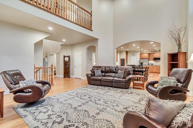 living room featuring arched walkways, light wood-style floors, a high ceiling, recessed lighting, and baseboards