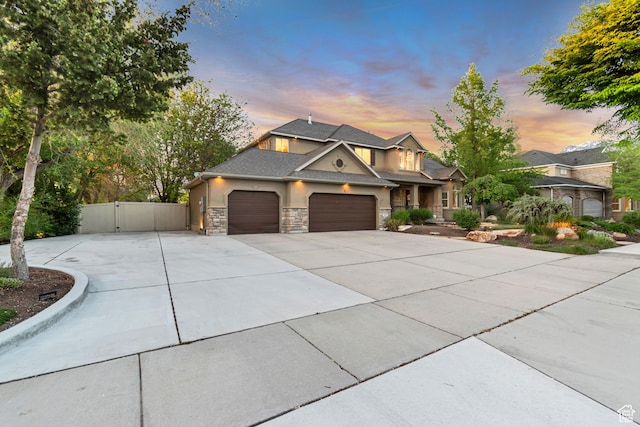 view of front of house with a gate, an attached garage, concrete driveway, stucco siding, and stone siding
