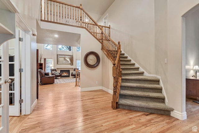 entrance foyer featuring wood finished floors, arched walkways, stairway, a glass covered fireplace, and a high ceiling