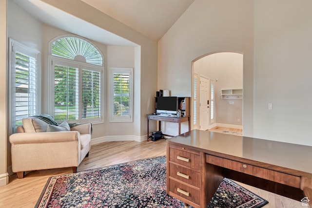 office space featuring arched walkways, light wood-style floors, baseboards, and lofted ceiling